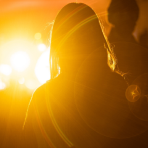 silhouette of a girl standing in front of a bright golden light as it shines on her