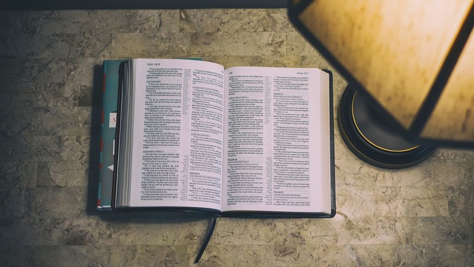 Bible open on a table next to a lamp