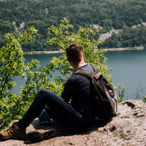 guy with backpack sitting on rock above river