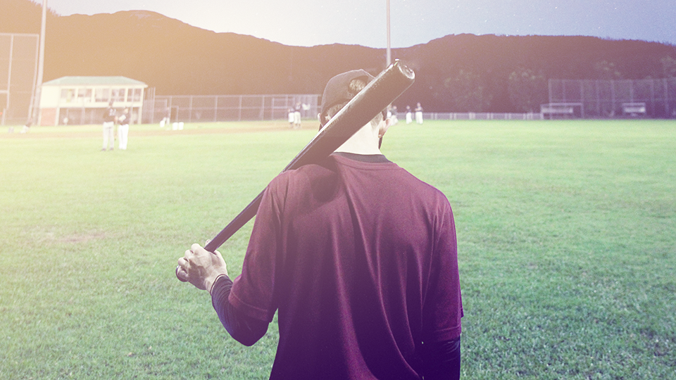 man holding baseball bat looking down on the field