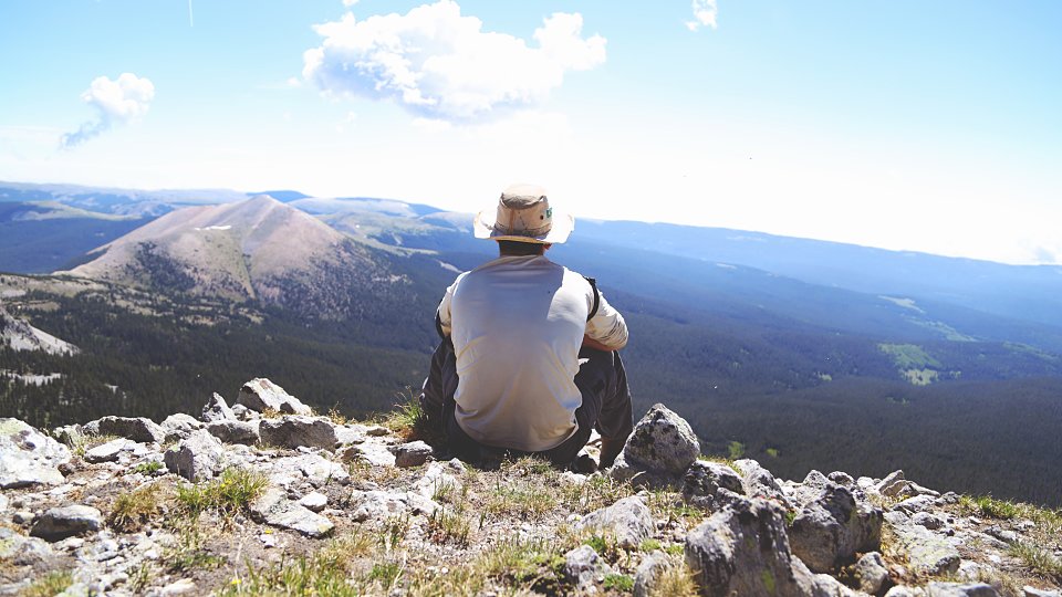 man sitting on a rocky mountain looking at land