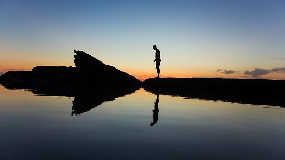man standing on rock in front of the sunset