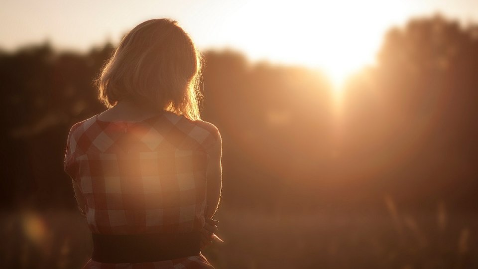 person standing with arms crossed looking at the sun setting