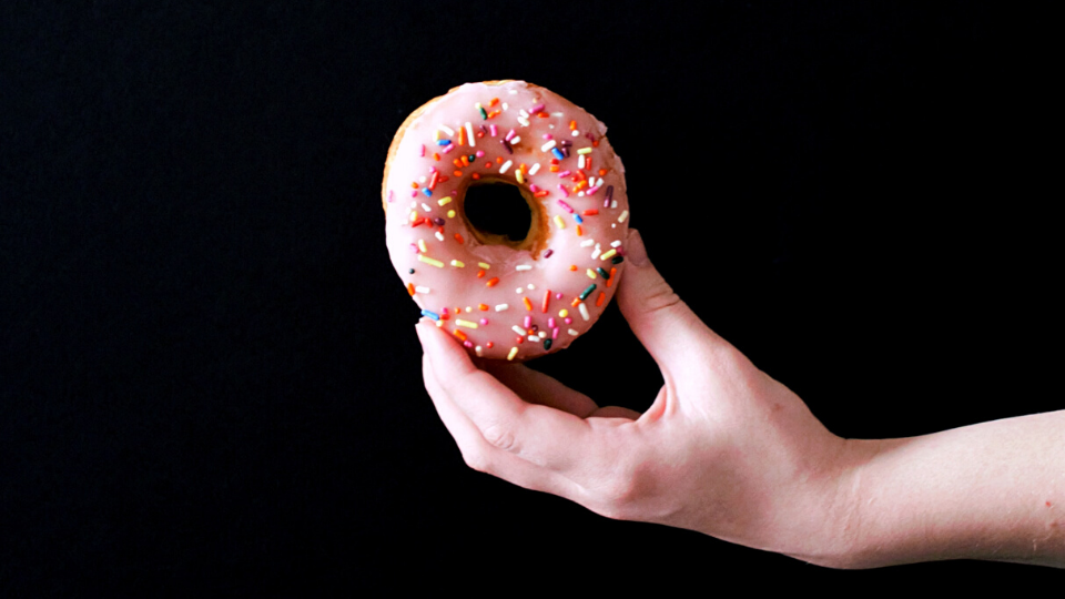 pink sprinkle donut being held in front of black background