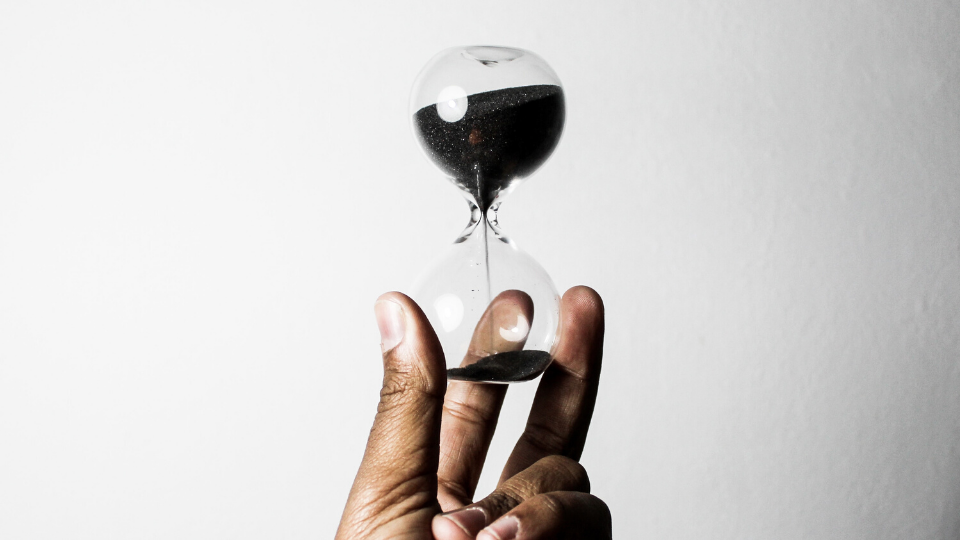 hand holding hourglass timer against a white, blank wall