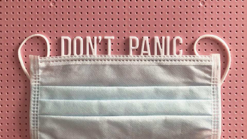 words "don't panic" spelled out on a letter board with a medical mask lining the bottom of them