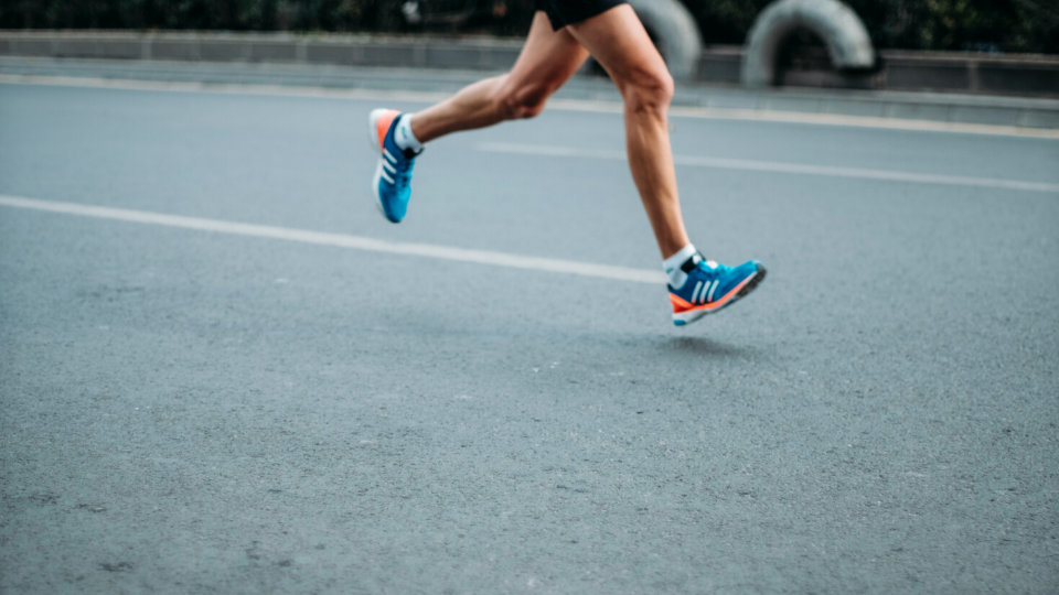 person's legs running on a black pavement road with blue tennis shoes on