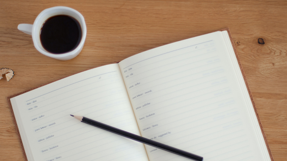 White planner laying on a light-wooden table with a coffee mug in the left hand corner