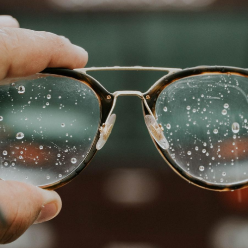 Person holding up glasses in front of camera with water droplets on the lenses