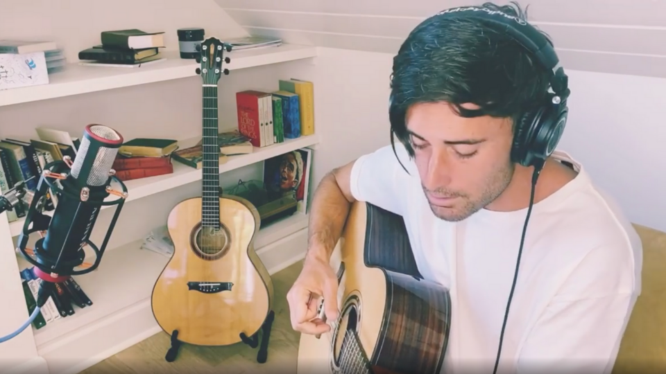 Phil Wickham sitting in the corner of a room in a white shirt with a microphone in front of him while wearing black headphones and a tan guitar