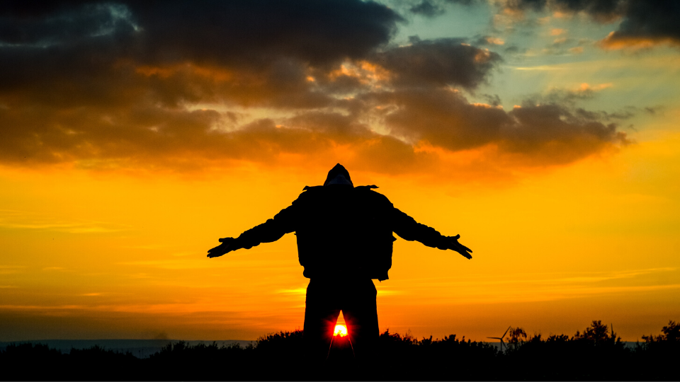 silhouette of a man holding his arms out and looking up with orange sunset in the background