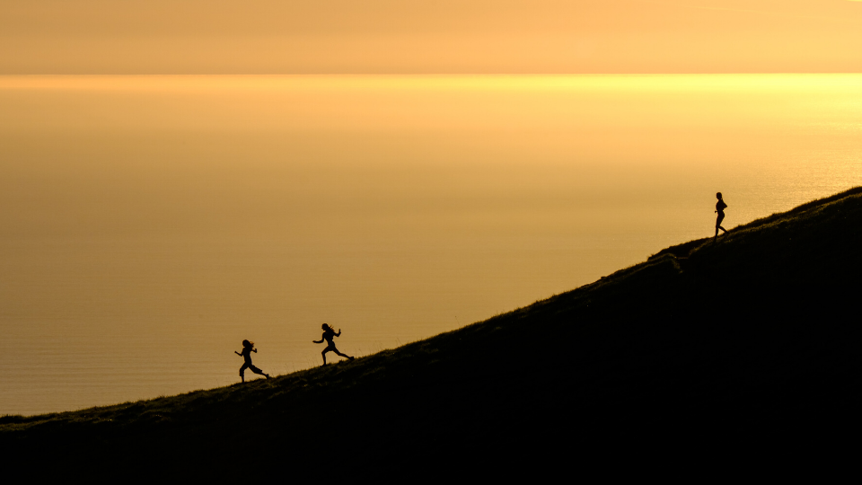 yellow sunset behind a hill and three people running down the hill