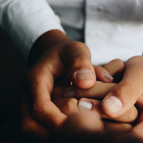 Parent holding a childs hand in between their own in a prayer position
