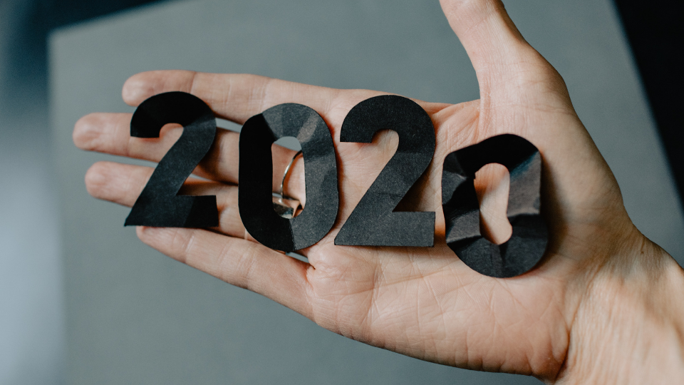 2020 cut out in black paper and crumpled up as it lays in the palm of a person's hand