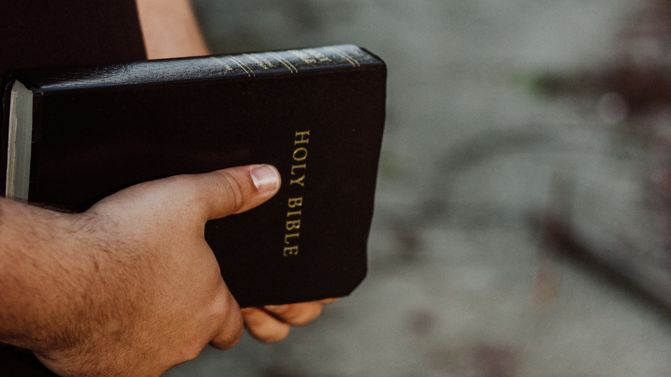 mans hands holding a black Bible with the words Holy Bible written in gold on the front