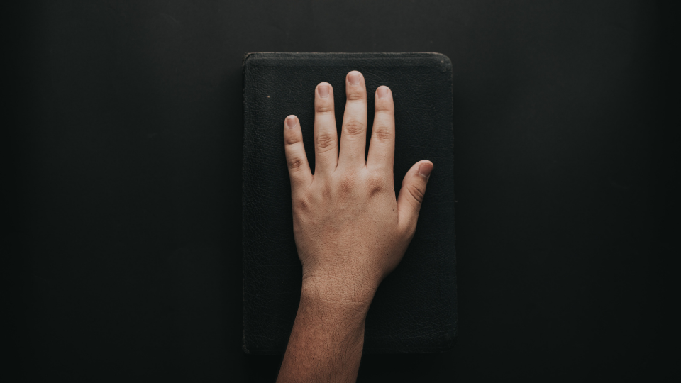 a black background with a flat hand resting on a black Bible
