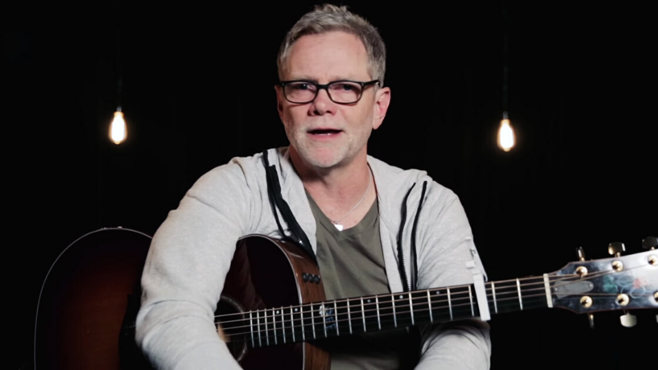 Steven Curtis Chapman sitting in a grey zip up hoodie with his dark brown wooden guitar on his lap