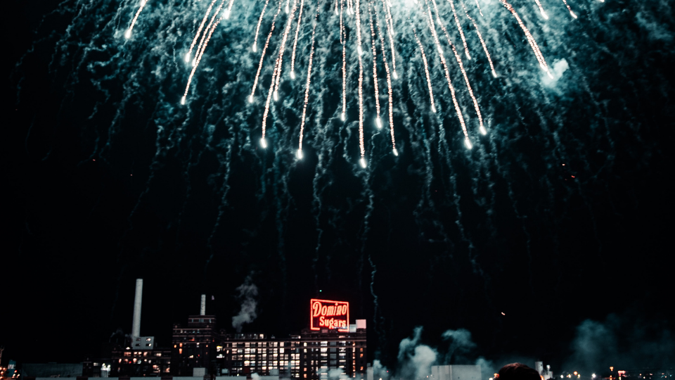 bright white fireworks showering down over the red domino sugar neon sign in Baltimore Maryland