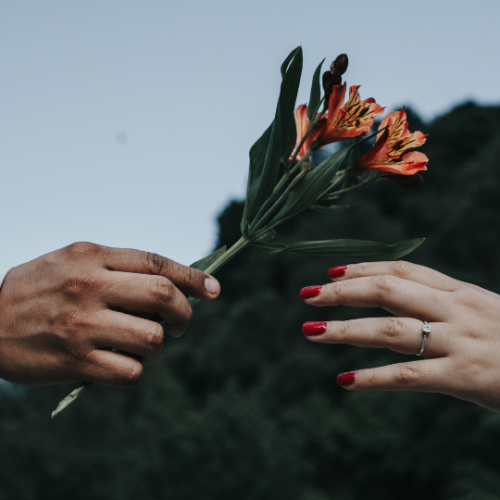 hand giving orange flowers to an open hand with red finger nails reaching towards the flowers