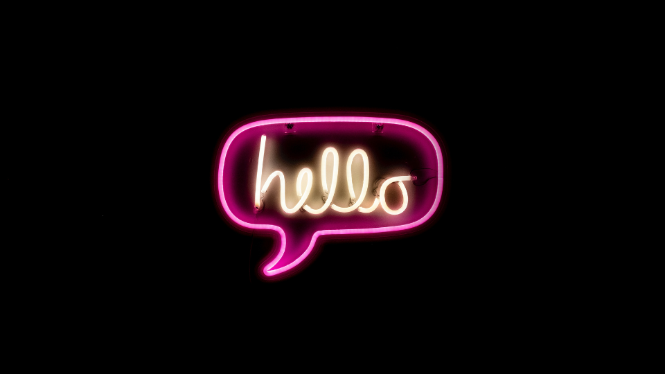 neon sign of a pink speech bubble with the word hello written in white cursive lights