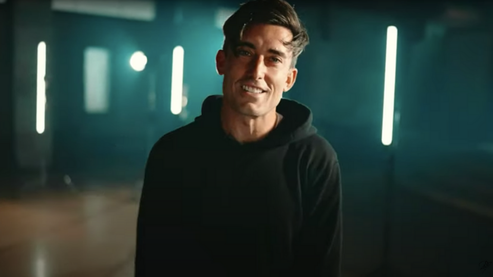 Phil Wickham standing in front of green fluorescent lights while smiling and wearing a black hooded sweatshirt