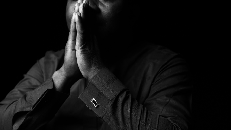 black and white picture of a man holding praying hands up to his mouth with his eyes closed