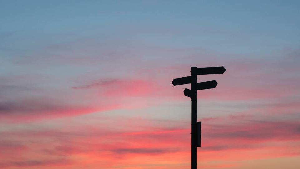 pink blue and purple sky with a sign in front of it with arrows pointing different directions