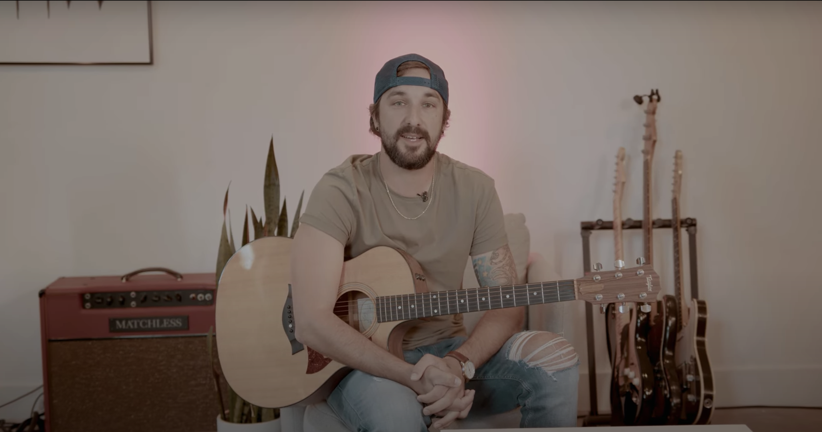 Rhett Walker sitting in a chair against a white wall while wearing a tan shirt and holding a wooden acoustic guitar