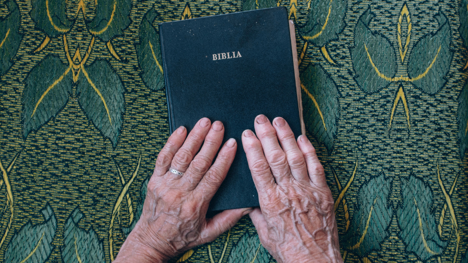 hands of an older person resting on a black Spanish Bible