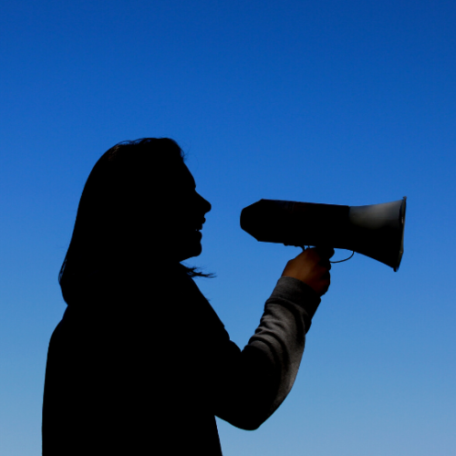 silhouette of a girl standing against a blue sly while holding a megaphone to her mouth