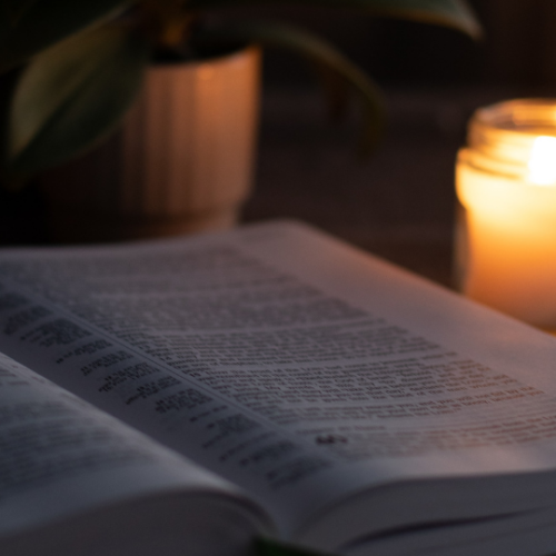 open Bible in the dark with a small white candle sitting on the right illuminating it