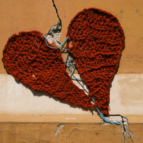 crack in a pale orange wall that has a knitted heart torn in half placed over the crack