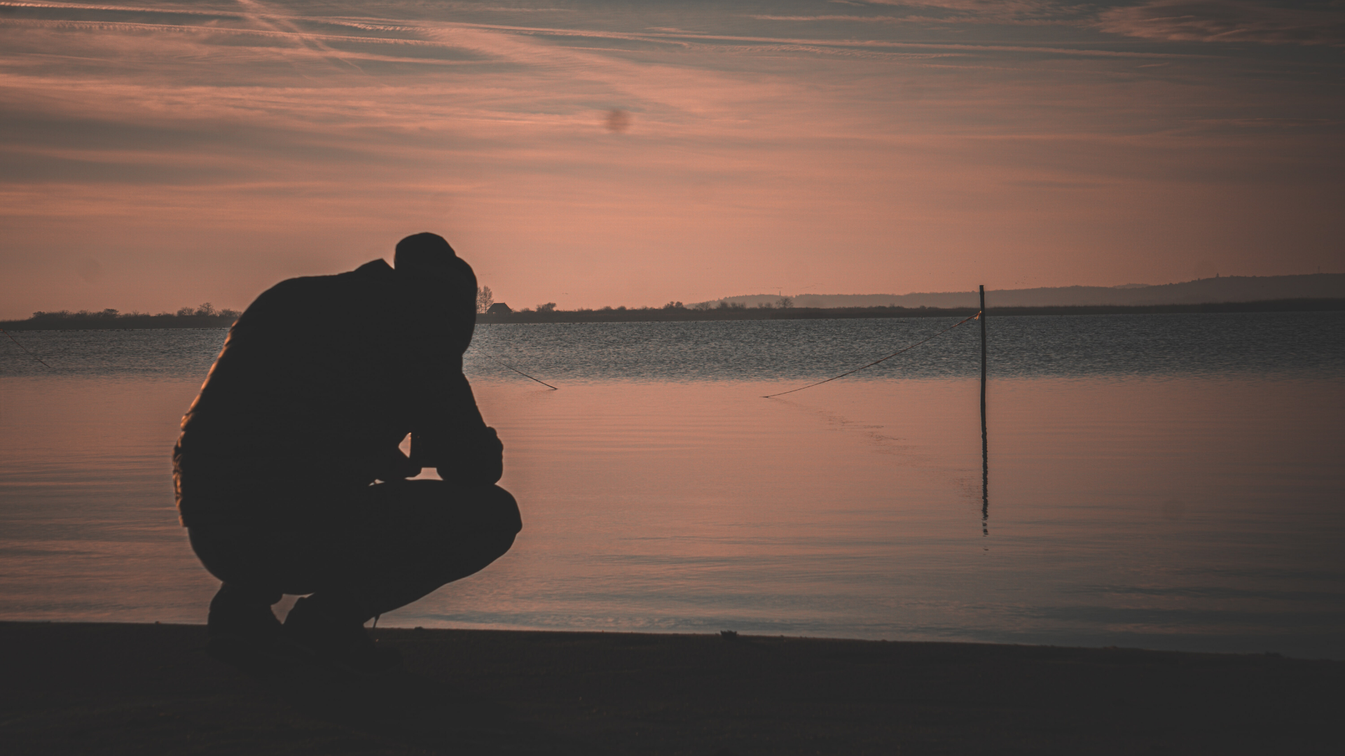 man crouched down near a body of water with his head looking down