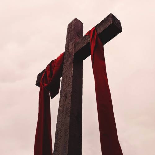 camera pointing up at a tall wooden cross with a dark red fabric draped over it