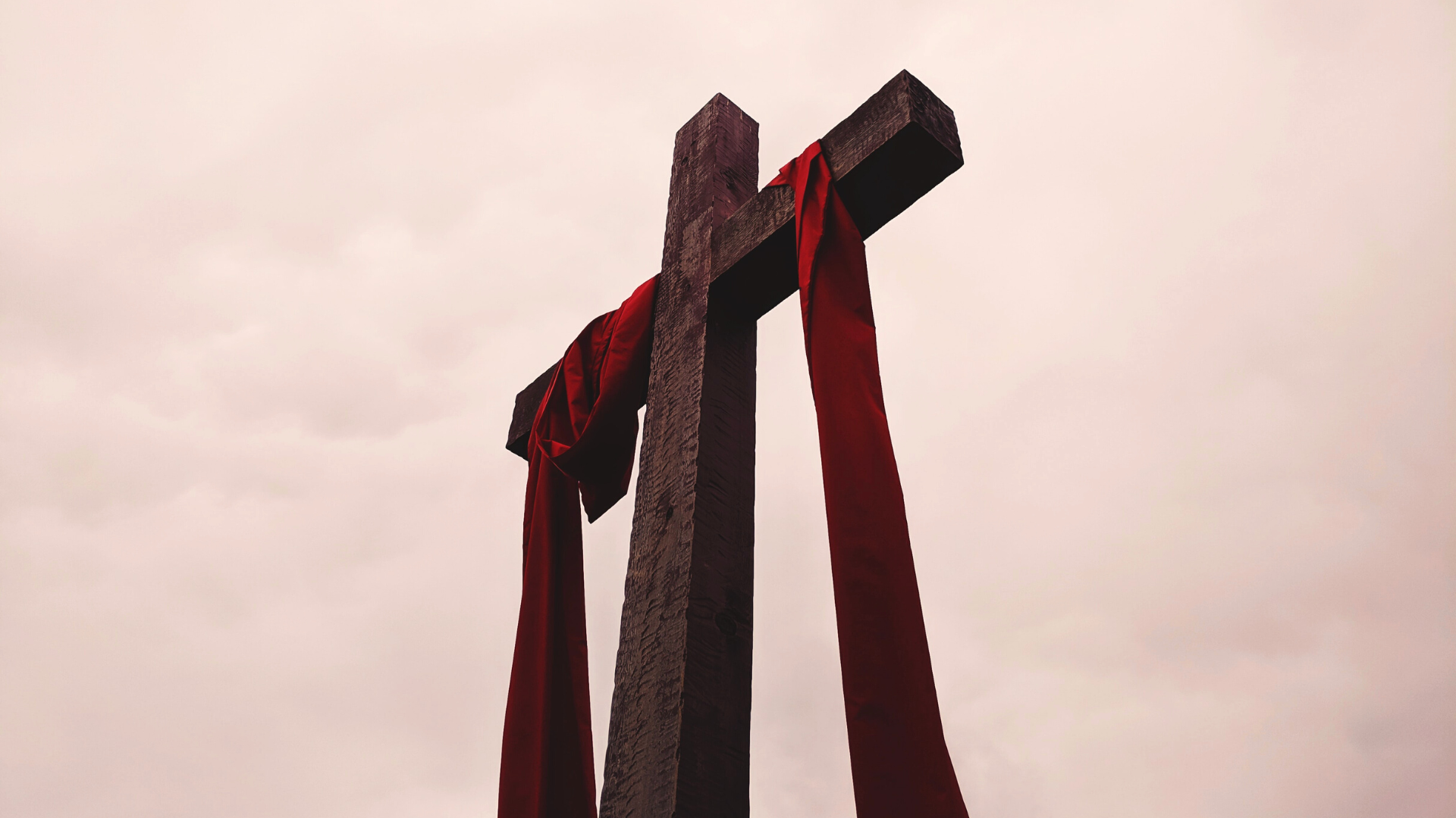camera pointing up at a tall wooden cross with a dark red fabric draped over it