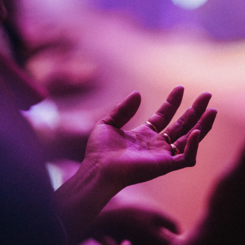 purple light shining down on someone's hands as they're holding them out to worship