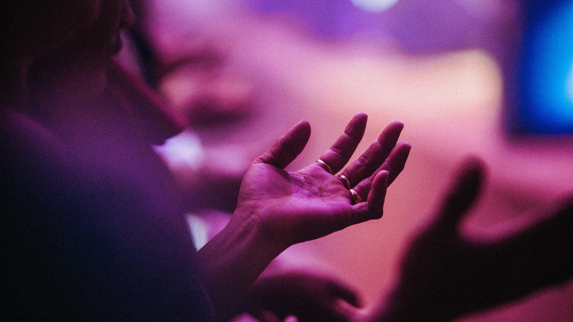 purple light shining down on someone's hands as they're holding them out to worship