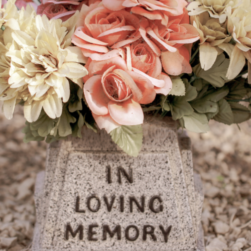 a tombstone that reads "In Loving Memory" with pink, white, and purple flowers placed on it