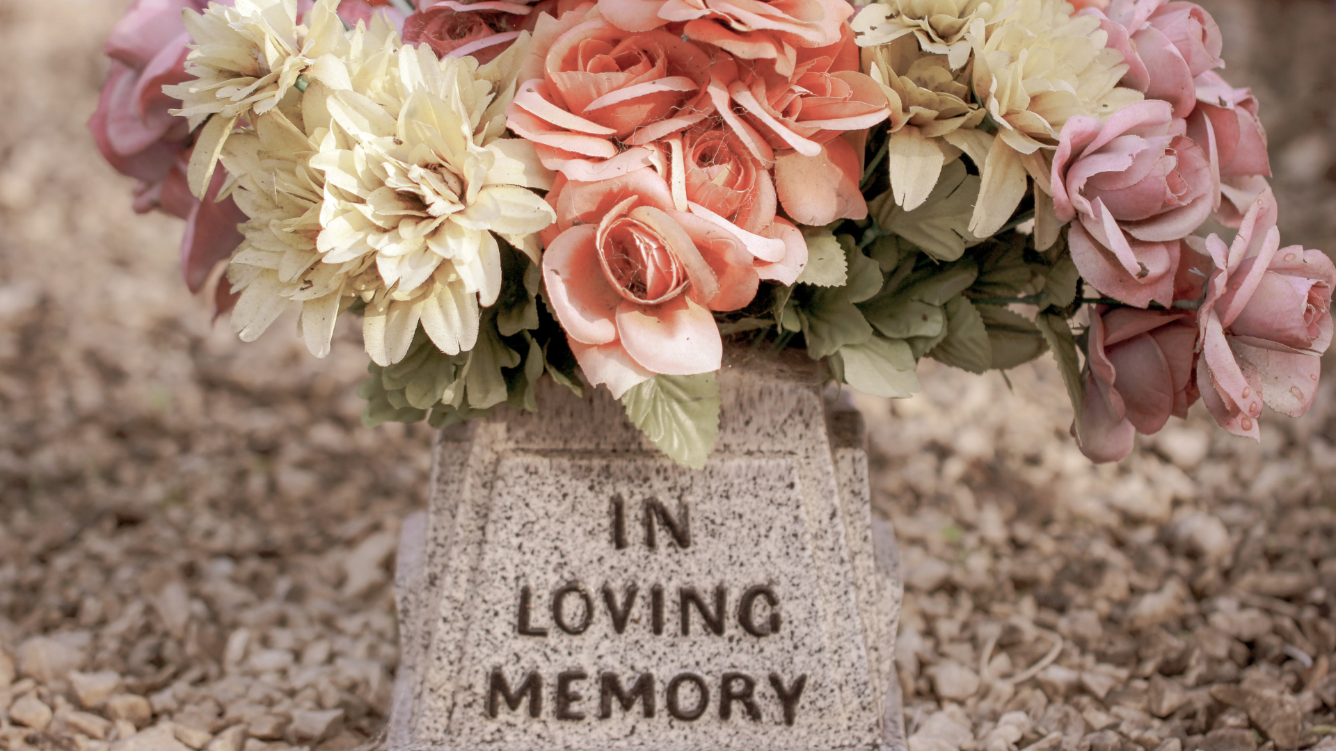 a tombstone that reads "In Loving Memory" with pink, white, and purple flowers placed on it