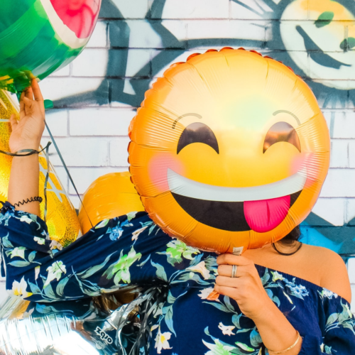girl holding a smiling emoji balloon in front of her face