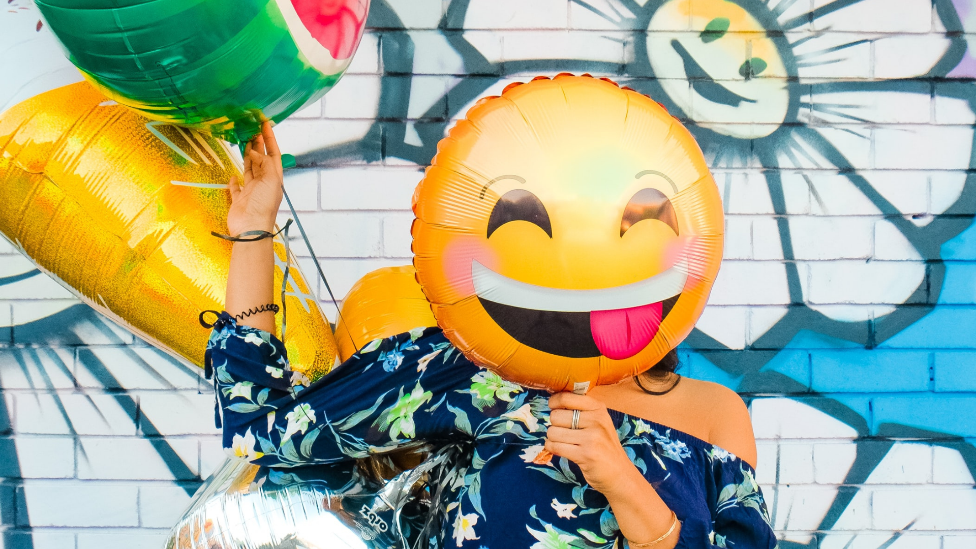 girl holding a smiling emoji balloon in front of her face