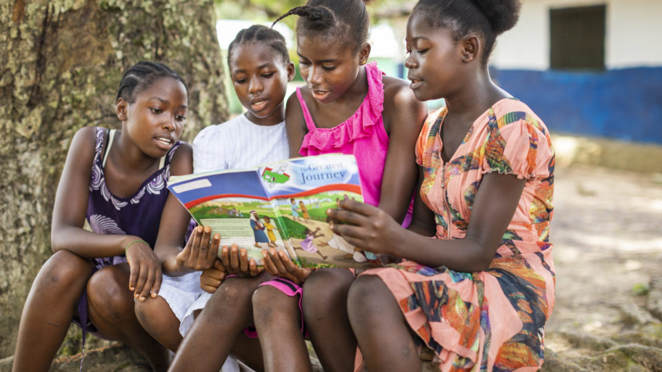Four girls in Liberia gather under a tree to read The Greatest Journey with 12 engaging lessons teaching them how to follow Christ and share Him with friends and family.