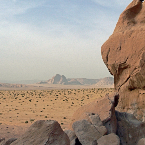 landscape of a dry desert with rocks in the foreground and a mountain in the distance against a pale blue sky