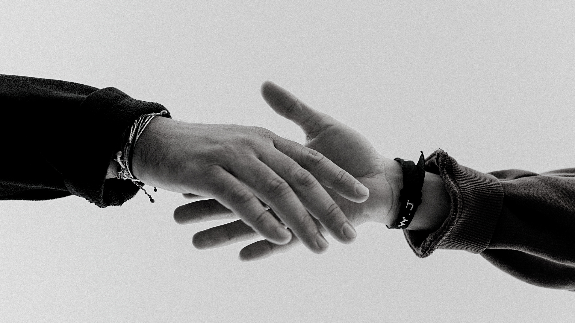 black and white picture of two hands reaching from different sides to hold one another's hand
