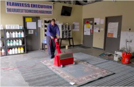 person using a large red machine to clean a rectangular area rug