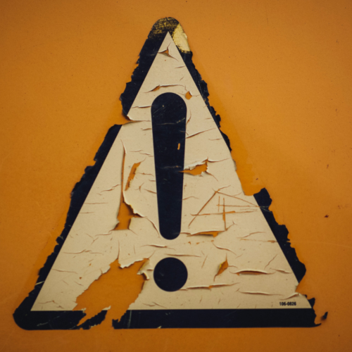 a peeling warning sign stuck to a yellow wall