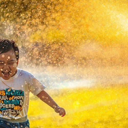 Little boy laughing and running through sprinkler