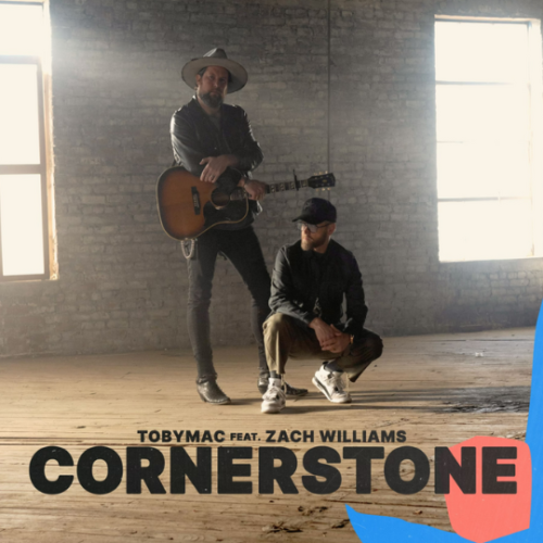 Zach Williams standing with arms crossed and a guitar slung across him as Toby Mac kneels on the ground and looks to his right