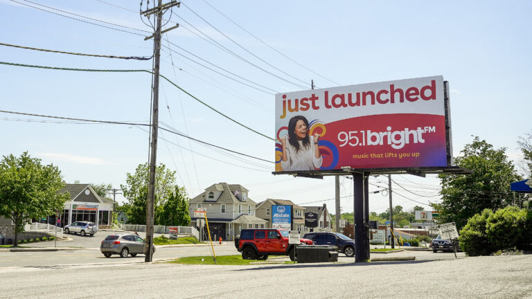 Billboard with smiling woman announcing BRIGHT-FM has just launched.