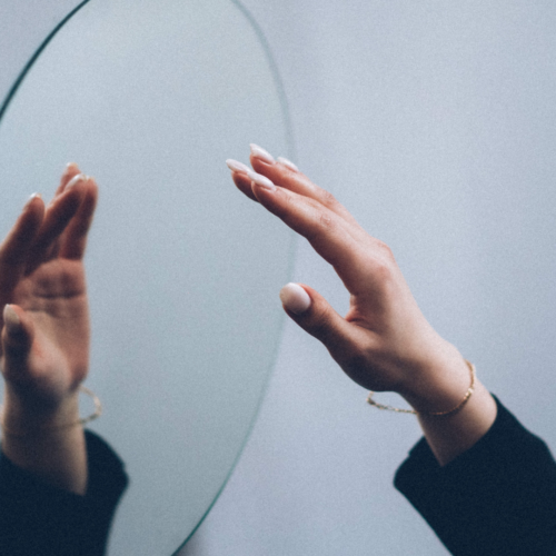circle mirror hanging on a grey wall and a person's hand reaching up to the mirror